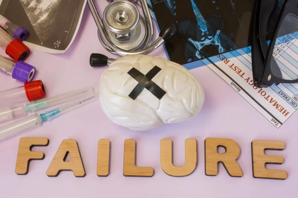 Brain, mental or cognitive failure concept photo. Brain with glued black cross is near word failure and set of medical tests (MRI, ultrasound, analysis), diagnostic devices (stethoscope, test tubes)