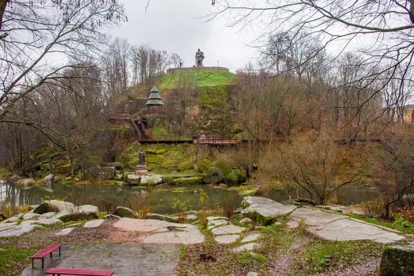 Hill near stone granite canyon of river Uzh in park with monuments to heroes and personalities of ancient Kievan Rus and ancient Drevlyanians amid of autumn gray rainy sky and wet weather in Korosten