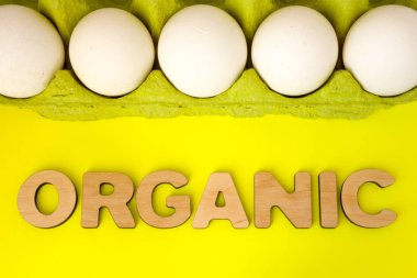 Organik gıda - tavuk yumurtası kavram resmi. Organik, doğal ahşap 3d harflerin oluşan kelime bir sarı zemin üzerine yeşil karton ambalaj içinde tavuk yumurta vardır