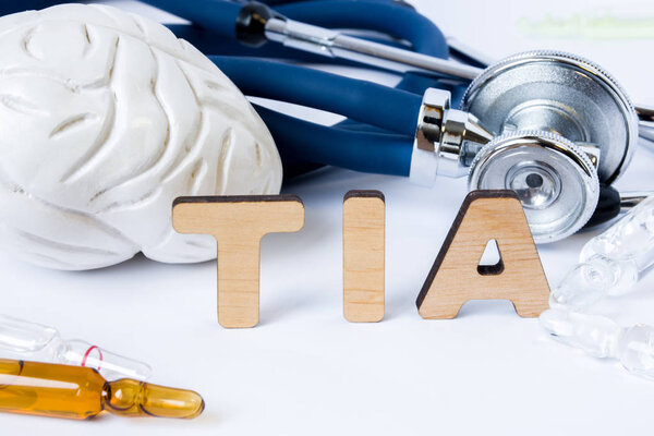 TIA Acronym or abbreviation to medical concept or diagnosis of transient ischemic attack or small brain stroke. Word TIA stands among models of the brain, stethoscope and medicines in ampules or vials