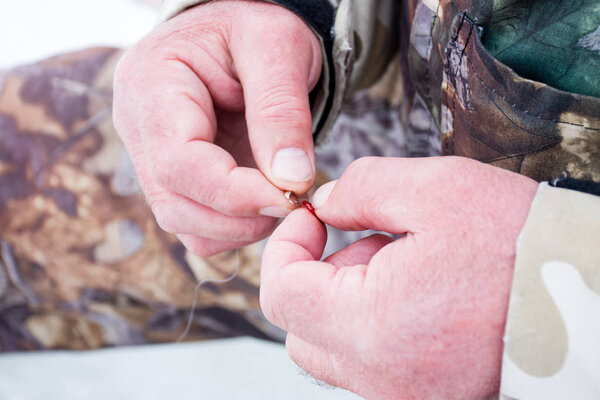 Fisherman puts jig bait on the mormyshkas hook to catch fish in winter with ice - bloodworms or mosquito larvae. Picture the scene with winter fishing on the ice using tackles