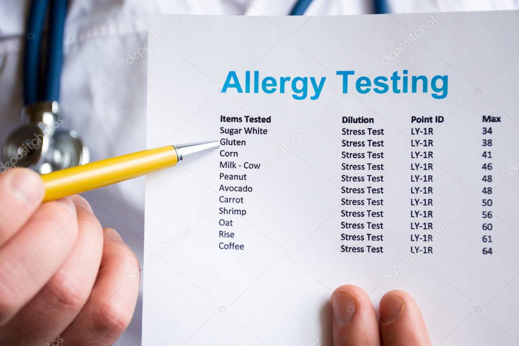 Analysis and testing for allergies photo concept. Doctor points with pen in his hand on result of patient allergy test in foreground, standing in medical gown with stethoscope in blurred background