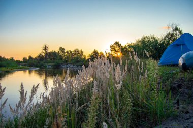 Sabah şafak vakti turist kampında ya da balıkçı tekneyle nehirde rafting yaptıktan sonra. Yüksek kıyıda duran şişme teknenin yanındaki turist çadırı. Ukrayna 'daki Teteriv Nehri. Seyahat, açık hava ve macera 