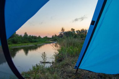 Güneşin doğuşu, bulutsuz açık gökyüzü mavi, kırmızı ve mor renkler, yüksek kıyıdan nehre doğru gün doğumu turist gözü menzilinde açık körfez çadırıyla. Ukrayna 'daki Teteriv Nehri