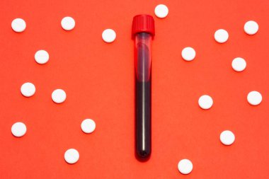 Üzerinde kan olan laboratuvar tüpü kırmızı zeminde beyaz tabletlerle çevrili ve süsü puantiyeli. Tıp, hematoloji, kan hastalıklarının teşhisi için resim konsepti
