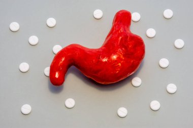 Midesinin anatomik şekli, canlı organın aynı şekli, beyaz haplarla çevrili gri arka planda, polka noktaları süslemesi. Gastroenterolojide kullanmak için fotoğraflar, tedavi için konsept 