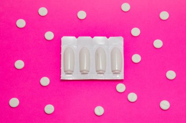 Vajinal veya rektal fitilli plastik ambalaj pembe arka planda polka noktalarıyla süslenmiş yuvarlak tabletlerle çevrilidir. Proktolojik ya da jinekolojik fotoğraf tedavisi kavramı