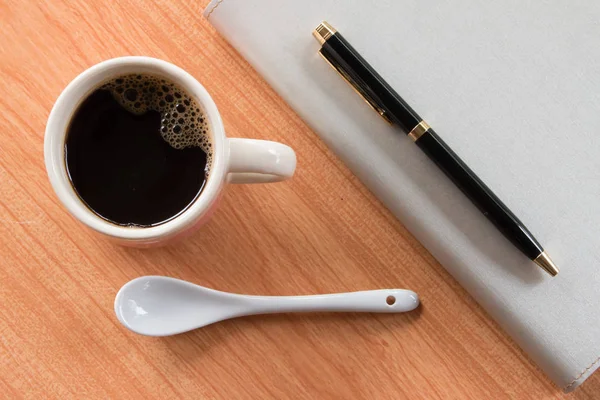 Fincan kahve kaşık ile ve defter kalem ahşap Resepsiyon arka plan üzerinde ile