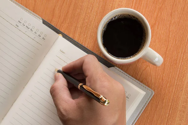 Mano del hombre escribiendo en cuaderno abierto con café caliente — Foto de Stock