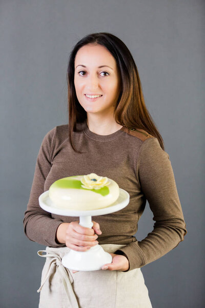 Portrait of young pastre shef with cake on gray background.