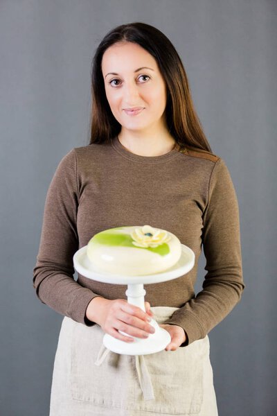 Portrait of young pastre shef with cake on gray background.