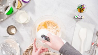 Düz yatıyordu. Adım adım. Vanilyalı Mardi Gras kekleri pişirmek için karışımı elektrikli mikserle karıştırıyorum..