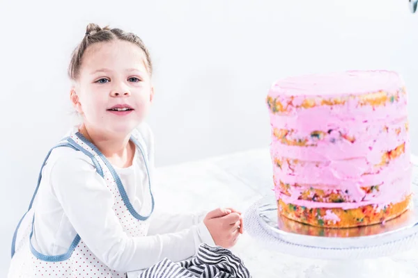Маленька Дівчинка Допомагає Спекти Високий Кумедний Торт Рожевим Масляним Кремом — стокове фото