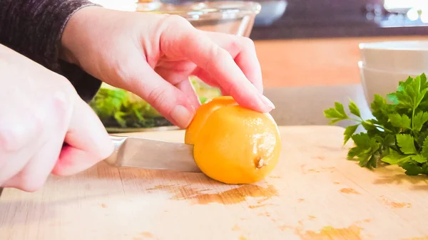 Slicing organic lemon on wood cutting board.