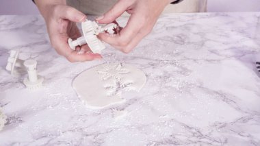 Adım adım. Mermer tezgahın üzerindeki beyaz fondanla kar tanelerini keserek..