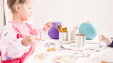 Adım adım. Küçük kız Cadılar Bayramı balkabaklarını süslemek için deniz kızı kuyruğu ve deniz kabuklarını akrilik boyayla boyuyor..