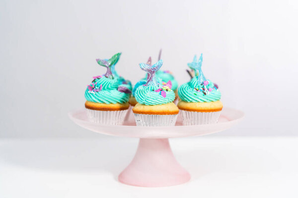 Gourmet mermaid cupcakes topped with blue buttercream frosting and decorated with sprinkles and chocolate mermaid tails.