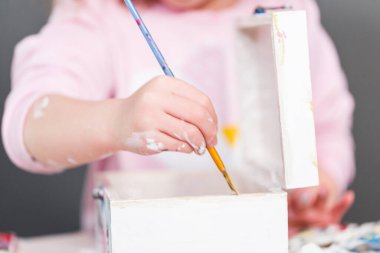 Küçük kız akrilik boya ile tahta bir kutu üzerinde bir tek boynuzlu at boyama.