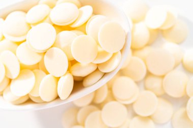 Beyaz arka planda çikolata şekillerini eritmek için beyaz yuvarlak çikolata parçaları..