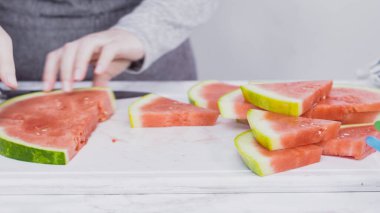 Kırmızı karpuzu beyaz bir kesme tahtasının üzerinde küçük parçalara ayırmak.