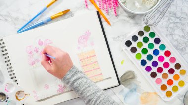 Düz yatıyordu. Baker suluboyalı bir doğum günü pastası çiziyor..