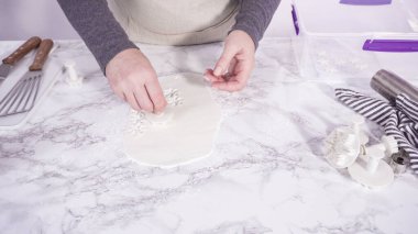 Adım adım. Mermer tezgahın üzerindeki beyaz fondanla kar tanelerini keserek..