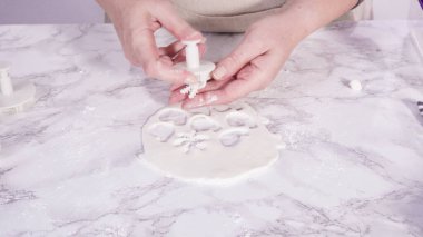 Adım adım. Mermer tezgahın üzerindeki beyaz fondanla kar tanelerini keserek..