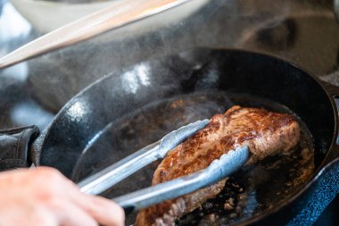 Elektrikli fırının üstünde kızgın demir tavayla New York bifteği kızartıyorum..