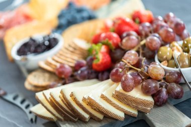 Aperatif olarak sunulan tahtanın üzerinde gurme peyniri, kraker ve meyve var..