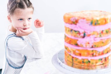 Pembe kremalı uzun funfetti keki pişirmeye yardım eden küçük kız..