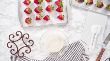 Düz yatıyordu. Adım adım. Çikolata kaplı çilek hazırlamak için organik çilekleri erimiş çikolatayla bir kaseye daldırmak..