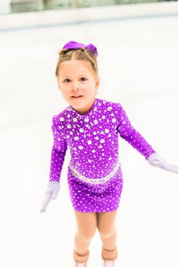 Mor elbiseyle buz pateni pistinde kristallerle buz pateni antrenmanı yapan küçük bir kız..