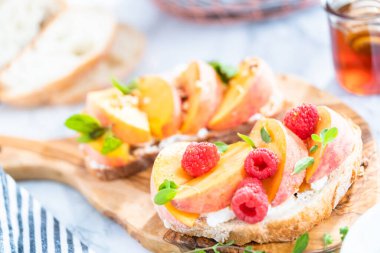 Şeftalili ricotta tostları ceviz, taze nane ve ahududu ile süslenmiş ahşap kesim tahtasında..