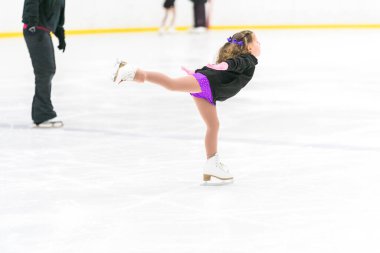 Küçük kız buz pateni pistinde artistik patinaj yapıyor..