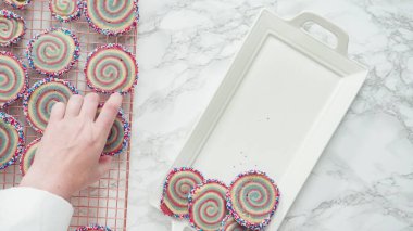 Adım adım. Düz yatıyordu. Beyaz servis tepsisinde kırmızı, beyaz ve mavi fırıldak şekerli kurabiyeler düzenleniyor..