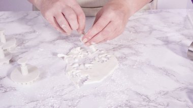 Adım adım. Mermer tezgahın üzerindeki beyaz fondanla kar tanelerini keserek..