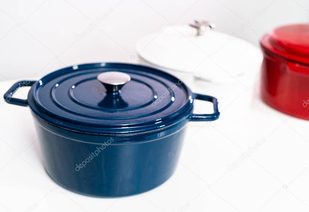 Red, white and blue enameled cast iron covered round dutch ovens on a whjite background.