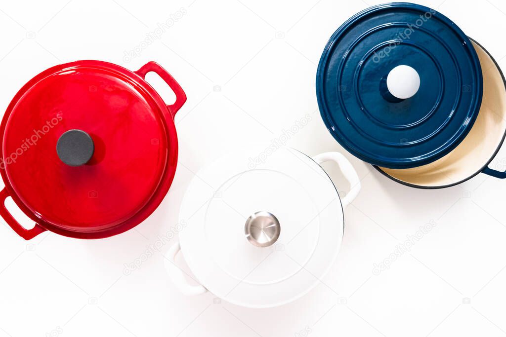 Flat lay. Red, white and blue enameled cast iron covered round dutch ovens on a whjite background.