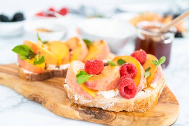 Beyaz tabakta böğürtlenlerle süslenmiş şeftalili ricotta tostu.