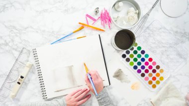 Düz yatıyordu. Baker suluboyalı bir doğum günü pastası çiziyor..