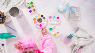 Düz yatıyordu. Küçük kız evde eğitim projesi için akrilik boyayla heykelcikler boyuyor..