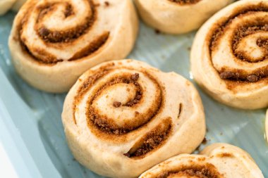 Fırınlanmamış tarçınlı çörekler mavi bir tavada.