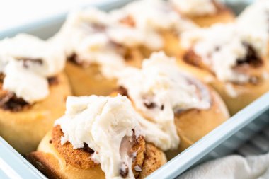 Taze pişmiş tarçınlı rulo, beyaz kremalı, mavi bir tavada..