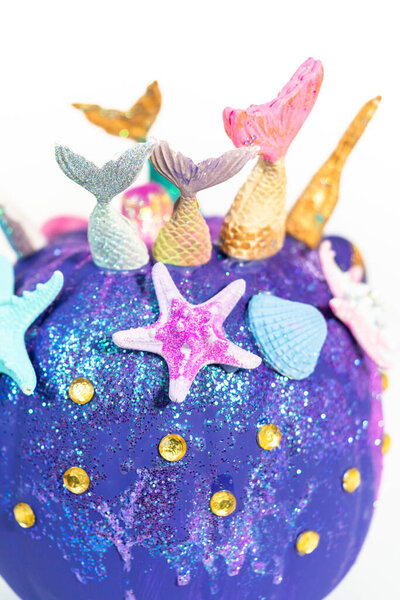 Halloween craft pumpkins decorated with mermaid tails, glitter, and sparkly rhinestones on a white background.