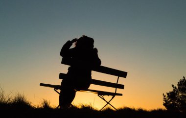 Günbatımı bir bankta oturan bir kişinin silüeti