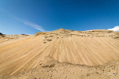 Mavi gökyüzü ve beyaz bulutlar gibi bir dağ tepe görünüyor arka planda büyük bir kum çukurunda kum
