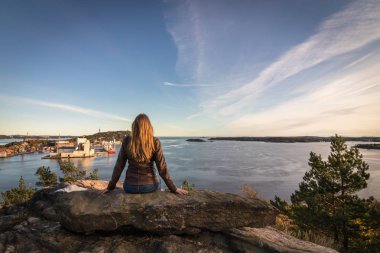 Fiyort ve Kristiansand şehirde bakarak bir kayaya oturan kadın.