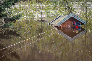 Small cabin floating in the water, tied with a rope. Flooding from the river Tovdalselva in Kristiansand, Norway - October 3, 2017. clipart