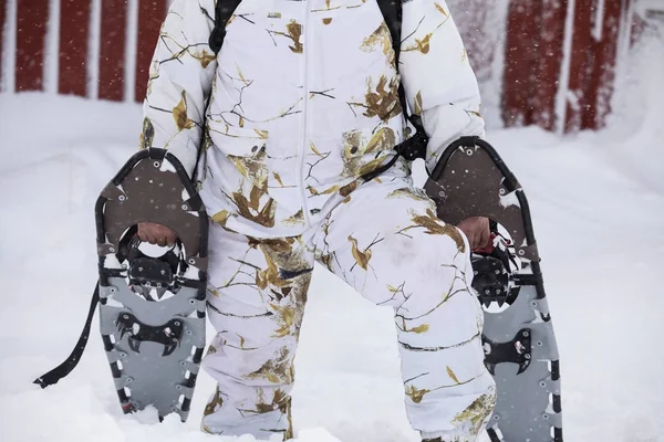 冬のスノーシューイング。冬に服を着ている男は雪の中、赤い小屋の外でスノーシューを抱えていた。頭なし — ストック写真