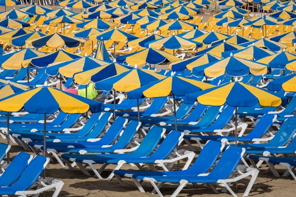 Rzędy niebieski leżaki z parasolami niebieski i żółty na plaży Playa de Puerto Rico na Wyspy Kanaryjskie — Zdjęcie stockowe